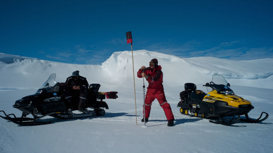 Drilling the ice and marking the spot for scientific research program with a flag on a bamboo stick for easy identification